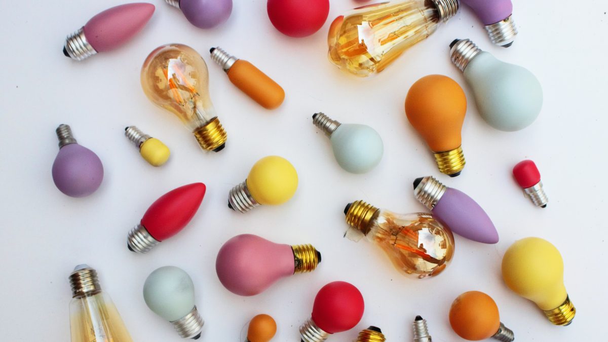 Selection of differently coloured lightbulbs lying on white floor