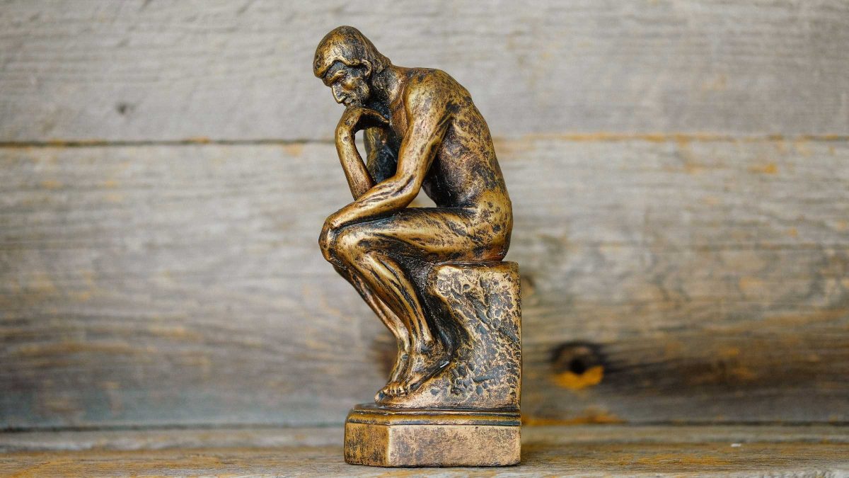 Picture of bronze statue of a man kneeling in a thinking pose