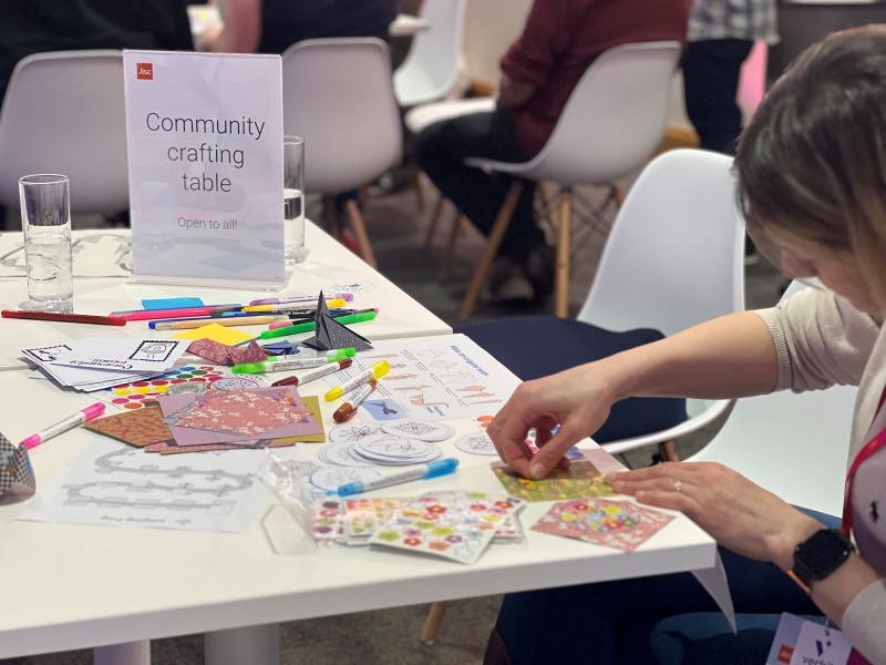 Image of person at a table filled wtih different crafts putting stickers on a piece of paper
