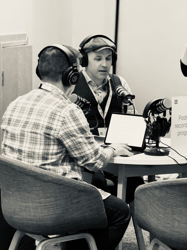 Black and white photo of two men recording a podcast, wearing headsets.